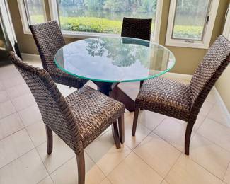 Five-piece dining set includes a round table with clear glass top and dark wood cross base, paired with four matching high-back chairs featuring dark brown woven wicker seats and backs over dark wood legs.