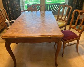 This piece is a classic French Provincial style dining table characterized by its elegant blend of rustic farmhouse charm & refined Louis XV design. The tabletop features an intricate geometric parquetry inlay crafted from solid oak. Draw leaf extensions on both ends allow for the table to significantly increase seating capacity. 6 matching chairs that have been recovered.