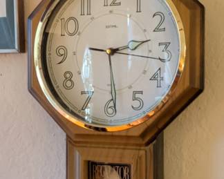 Made by Justime, featuring a battery-operated quartz movement with a brass pendulum. Design: Classic octagonal schoolhouse/regulator style with a faux wood/oak-finish case, gold-tone brass bezel, and lower glass window displaying "REGULATOR."
