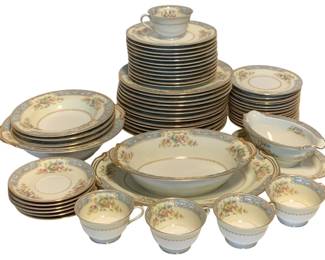 99 - 58pc Noritake China Set "Blue Dawn" (Description): A 58-piece Noritake china set featuring a delicate floral pattern with multicolored blooms. The pieces are accented with a light blue border, gilt trim, and a scalloped gold edge design. The set includes dinner plates, salad plates, bread plates, cups, saucers, a large oval serving bowl, a gravy boat with attached underplate, and additional serving pieces. The classic design features pink, yellow, and blue flowers arranged in bouquets