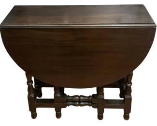 110 - Antique Walnut Gateleg Drop-Leaf Oval Table (Description): Antique William and Mary style drop-side gateleg table featuring a dark mahogany finish. The table showcases classic turned legs with decorative turnings and a shaped stretcher base. The oval top features two drop leaves supported by swing-out gate legs. Shows typical age-related wear consistent with antique furniture. Measures 30"x44"x32".
