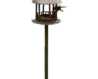 262 - Metal Pagoda Style Bird Feeder on Post 52" (Description): Metal bird feeder in a charming pagoda or gazebo style, mounted on a tall bamboo-style post. The feeder features an octagonal design with open lattice sides, a ribbed conical roof with a decorative finial, and a small perch for visiting birds. The piece displays a weathered patina consistent with outdoor use, with the roof showing light oxidation and the post finished in a dark green tone. Measures 52" tall.