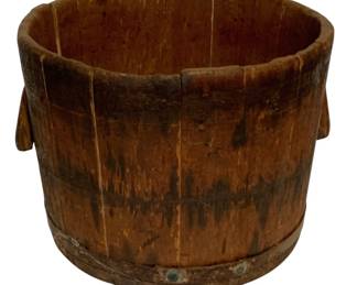 100 - Antique Wooden Bucket w/ Metal Band (Description): Antique wooden stave bucket featuring traditional construction with vertical wooden staves held together by an metal band at the base. The bucket includes two protruding wooden handles on opposite sides. The piece displays a rich patina and weathered surface consistent with age and use. Measures 10 1/2 inches by 13 inches.