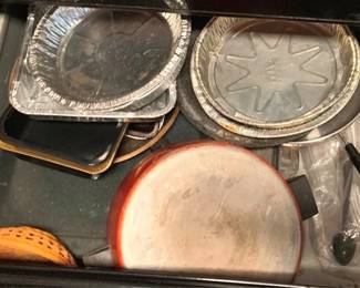 55 - Drawer Lot of Assorted Items (Description): A drawer lot of assorted pots, pans, and bakeware. The collection includes various aluminum baking pans, a ceramic or stoneware pizza stone with orange trim, assorted metal baking trays and roasting pans in different sizes, plastic utensils, and what appears to be a yellow ceramic colander or strainer. A practical kitchen assortment suitable for everyday cooking and baking needs.
