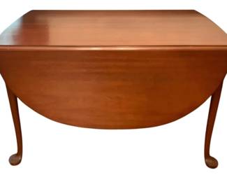 103 - Queen Anne Style Drop Leaf Table (Description): Queen Anne style drop leaf table in a warm cherry finish. The table features elegant cabriole legs with pad feet and two drop leaves that extend to create a generous oval dining surface. When fully extended, the table measures 30.5 inches tall by 69inches long by 53 inches wide. The classic design and rich wood tone make this piece suitable for both formal and casual dining settings.