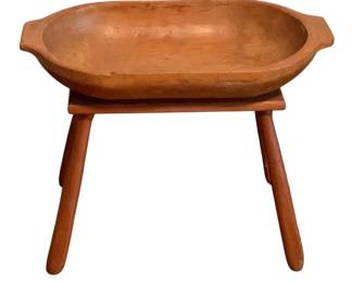 406 - Wooden Dough Bowl w/ Stand 20"x24"x12.5" (Description): A rustic wooden dough bowl with integrated stand. The hand-carved bowl features a warm honey-toned finish and traditional tab handles on either end. The stand consists of four splayed turned legs with stretcher supports, providing sturdy elevation for the bowl. Measures 20 inches by 24 inches by 12.5 inches overall.