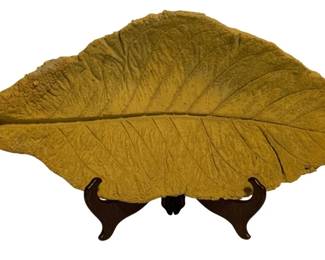 43 - Plaster Tobacco Leaf w/ Stand 10"x22" (Description): Decorative plaster tobacco leaf with display stand. The leaf features detailed vein impressions and texture, finished in a golden mustard yellow color that captures the natural appearance of a dried tobacco leaf. Comes with a dark wooden easel stand for display. Measures 10 inches by 22 inches.