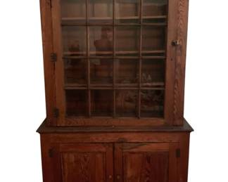 518 - Antique Cupboard 89"x51"x18" (Description): Antique cupboard crafted in oak with a warm, natural finish. This two-piece step-back cupboard features a glazed upper section with a single door divided into sixteen panes, providing excellent display space across multiple interior shelves. The lower cabinet section has two solid paneled doors with simple wooden knobs. The piece retains its original iron hardware including H-hinges and door latches. The cupboard rests on a shaped