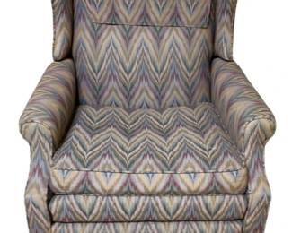 310 - Vtg Wingback Recliner w/ Flame Stitch Fabric (Description): Vintage wingback recliner upholstered in a classic flame stitch pattern fabric featuring muted tones of blue, mauve, gold, and cream. The chair features traditional rolled arms, high wingback design, and a skirted base. Measures 41 inches high by 31inches wide by 34 inches deep.