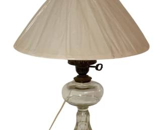 480 - Vtg Clear Glass Oil Lamp w/ White Shade 20" (Description): Vintage clear glass oil lamp measuring 20 inches tall. Features a pedestal base with a bulbous font, brass burner mechanism with adjusting key, and a pleated white glass cone shade with chimney. The lamp has been converted or styled for decorative display. Used as is electric/electronic/mechanical item. No guarantee all components, untested.