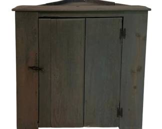 305 - Painted Hanging Primitive Corner Cabinet (Description): Painted hanging corner cabinet featuring a weathered blue-gray painted finish over pine wood construction. The cabinet has a peaked top crown and double plank doors with original iron strap hinges and a wooden turn latch closure. The piece exhibits a charming primitive, country style typical of 19th century American craftsmanship. Measures 36 inches by 36.5 inches by 25 inches.