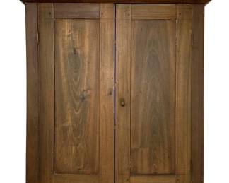 245 - Antique Hanging Wood Cabinet 40"x41"x31" (Description): Antique hanging wood cabinet featuring two paneled doors with raised panels and a simple brass knob closure. The cabinet displays warm brown tones with attractive natural wood grain throughout. Topped with a simple molded cornice, this rustic country-style piece shows authentic age and patina consistent with 19th century craftsmanship. Measures 40 inches by 41 inches by 31 inches.