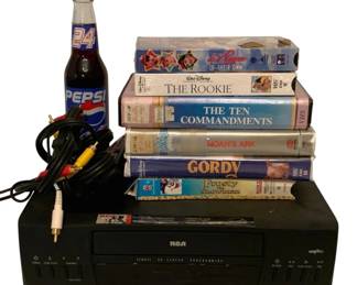 202 - RCA VCR Player w/ VHS Tapes & AV Cables (Description): This lot includes an RCA VCR player with VCRPlus+ programming capability, accompanied by a set of AV cables for connection. Also included is a collection of six VHS tapes featuring family-friendly titles including Walt Disney's The Rookie, Gordy, and Frosty the Snowman, as well as A League of Their Own, The Ten Commandments, and Noah's Ark. A collectible Pepsi bottle featuring the number 24 completes the lot.