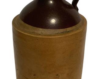 16 - Antique Two-Tone Stoneware Jug 9.5"x6" (Description): Antique two-tone stoneware jug featuring a dark brown Albany slip glaze on the shoulder and handle with a natural tan salt-glazed body. This classic American stoneware piece has a single loop handle and small pouring spout typical of 19th century whiskey or cider jugs. The jug measures 9.5 inches tall by 6 inches in diameter and shows authentic age-related wear consistent with its period of use.