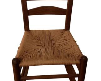 502 - Antique Ladder back Rocking Chair 33"x18"x27" (Description): Antique ladder back rocking chair featuring a traditional three-slat back design and a woven rush seat. The chair is constructed of warm-toned wood with turned finials atop the back posts and curved rockers at the base. The rush seat displays a classic radiating weave pattern. Measures 33 inches high by 18 inches wide by 27 inches deep.