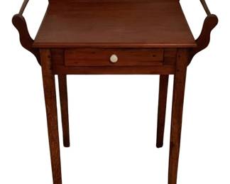 500 - One-Drawer Wash Stand 32"x27.5"x18" (Description): One-drawer wash stand crafted in warm-toned wood with a rich cherry or walnut finish. Features a shaped gallery backsplash with curved scrollwork sides, a single drawer with a white porcelain knob, and four tapered square legs. The piece exhibits classic American country or Federal style characteristics. Measures 32" x 27.5" x 18".