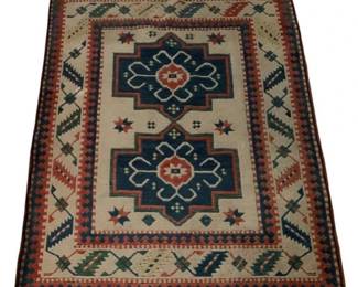 514 - Vtg Wool Kilim Rug 75"x51" (Description): Vintage Kazak style wool kilim rug featuring two central medallions in navy blue with coral and cream geometric motifs. The cream field is surrounded by multiple decorative borders incorporating traditional tribal patterns in blue, green, coral, andcream. Finished with fringe at both ends. Measures 75 inches by 51 inches.