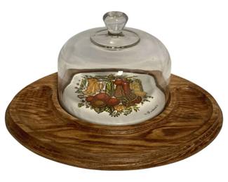 67 - Vtg Mid Century Serving Dish w/ Glass Dome (Description): Vintage Mid Century serving dish featuring a wooden base with a ceramic center tile decorated with a colorful harvest motif of canning jars, vegetables, and greenery. The set includes a clear glass dome with a knob handle. The wooden base has a warm oak finish with a carved groove around the ceramic insert. Measures 6" x 12" x 8".