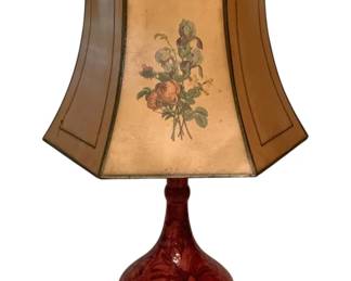 215 - Red Majolica Style Floral Table Lamp 25" (Description): A striking table lamp featuring a red majolica-style ceramic base with raised floral and leaf relief decoration. The bulbous gourd-shaped base sits on a brass foot and is topped with a distinctive hexagonal shade decorated with hand-painted botanical illustrations of roses and irises. The shade appears to be parchment or vellum with green trim detailing. Measures 25 inches in height.