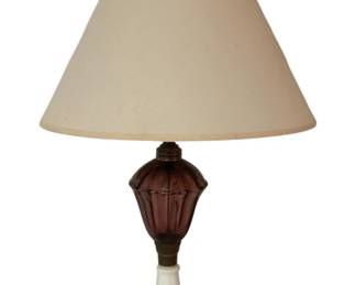 477 - Amethyst Glass & Milk Glass Base Table Lamp (Description): Elegant table lamp featuring an amethyst glass body with paneled design, mounted on a decorative milk glass base with scalloped edges and ribbed detailing. The lamp includes brass-tone fittings and is topped with a cream-colored fabric shade. Measures 22.5 inches tall. Used as is electric/electronic/mechanical item. No guarantee all components, untested.