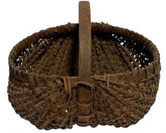 87 - Antique Woven Splint Buttocks Basket (Description): Antique woven splint buttocks basket featuring a sturdy bentwood handle. This handcrafted basket displays traditional construction with tightly woven oak splints in a classic ribbed pattern. The basket has developed a rich, warm brown patina consistent with age and use. Measures 14 inches by 14 inches by 15 inches including handle height.