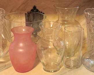 50 - Lot of Assorted Glass Vases (Description): A collection of assorted glass vases in various styles and sizes. The lot includes clear glass vases in different shapes including a footed vase with cut glass design, a tall flared vase, and several simple curved designs. One frosted pink glass bud vase is included among the clear pieces. A pressed glass vase with decorative pattern and a glass decanter are also part of this grouping.