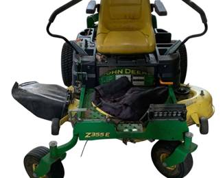 258 - John Deere Z355E Zero-Turn Riding Mower (Description): John Deere Z355E zero-turn riding mower featuring the classic green and yellow color scheme. This residential zero-turn mower is equipped with dual control levers for maneuverability, a cushioned high-back seat, side discharge chute, and front-mounted LED lights. The mower shows signs of use with some wear visible on the seat and deck areas. Includes a mulching cover on the deck. 36 x 78 x 61