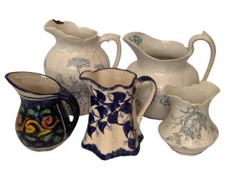 207 - Collection of Five Ceramic Pitchers & (Description): A collection of five ceramic pitchers and creamers in various styles and sizes. The grouping includes white ironstone pitchers with blue transfer ware floral designs, a blue and white vine-patterned creamer with scalloped edges, and a colorful hand-painted pitcher with folk art style orange, yellow, and green motifs on a dark blue ground. The pieces range from small creamers to larger serving pitchers, representing both antique