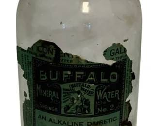 60 - Buffalo Mineral Water Bottle 11" (Description): Buffalo Mineral Water bottle measuring 11 inches. This clear glass bottle features a green and white paper label advertising Buffalo Mineral Springs natural spring water, described as an alkaline diuretic. The bottle has a silver metal screw cap and retains its original label, though with some wear and loss consistent with age. The label indicates the water was bottled in Buffalo, NY.