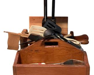 81 - Assorted Kitchen Utensils w/ Wooden Carriers (Description): A collection of assorted kitchen items including various cooking utensils such as spatulas, ladles, and tongs in both plastic and metal. The lot includes wooden kitchen accessories and carriers, featuring a wooden tray with handle cutout, a knife block with black handles, and additional wooden storage pieces. A variety of serving and cooking implements are included in this functional kitchen lot.