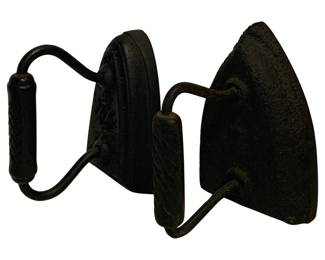 84 - 2 Antique SAD Irons 5"x6"x4" (Description): A pair of antique SAD irons featuring classic cast iron construction with curved metal handles. These traditional flat irons display a dark, aged patina consistent with their age and use. One iron features a twisted wire handle with a textured grip, while the other has a simple curved wire handle. The pointed soleplate design is characteristic of 19th century pressing irons. Each iron measures approximately 5 inches by 6 inches by 4
