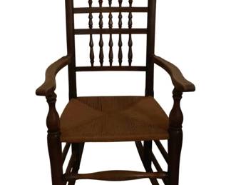 463 - Antique Spindle Back Rocking Chair Rush Seat (Description): Antique rocking chair featuring a spindle back design with turned wooden spindles arranged in two tiers. The chair has curved arms supported by turned arm posts and a traditional rush woven seat. The dark-stained wooden frame includes turned front legs and curved rockers connected by stretchers. Measures 44 inches high by 24 inches wide by 26 inches deep.