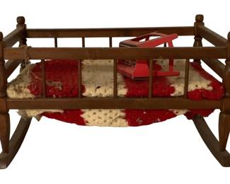 496 - Doll Size Wooden Rocking Cradle 13"x11"x18" (Description): Vintage doll size wooden rocking cradle with turned spindle rails and ball finial posts. The cradle features a traditional rocking base and includes a red and white crocheted blanket. Measures 13" x 11" x 18".