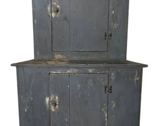 239 - Primitive Painted Corner Cupboard 73"x39"x22" (Description): Painted corner cupboard in blue-gray paint with desirable aged patina and surface wear. This two-piece cupboard features an upper section with a single door and lower section with a single door, both fitted with turned wooden knobs and iron hinges. The lower section displays a shaped apron base. Measures 73 inches tall by 39 inches wide by 22 inches deep.