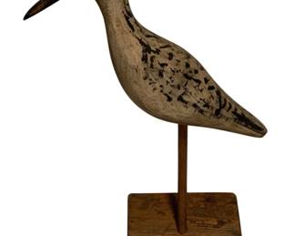 58 - Carved Wood Shorebird Decoy on Stand Signed (Description): Carved wood shorebird decoy mounted on a square wooden base. The bird features a long, slender beak and weathered painted surface with black spotting on the back and wings, giving it a realistic sandpiper or plover appearance. The piece is signed and displays charming folk art character with its aged, distressed finish. Measures 13.5" x 8.5" x 4".