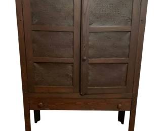 513 - Antique Punched Tin Pie Safe 58.5"x42"x16" (Description): Antique punched tin pie safe featuring two doors with decorative punched tin panels in a traditional star or geometric pattern. The cabinet is constructed of dark-stained wood, likely oak, with a single drawer at the base and stands on four tapered legs. The piece showcases classic American country craftsmanship typical of 19th century pie safes, where the punched tin allowed for ventilation while keeping pests away from
