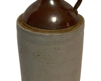 15 - Antique Two-Tone Stoneware Jug 7.5"x4.5" (Description): Antique stoneware jug featuring a classic two-tone design with a brown Albany slip glazed top and natural salt-glazed gray body. The jug has a single applied loop handle and retains its original cork stopper. This traditional American stoneware piece displays characteristic period construction with a rounded shoulder transitioning to a cylindrical base. Measures 7.5 inches tall by 4.5 inches in diameter.