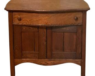 147 - Antique Oak Washstand w/ Drawer & Cabinet (Description): Antique oak washstand featuring a serpentine front drawer with two wooden knob pulls and a lower cabinet with paneled double doors. The piece displays beautiful quarter-sawn oak grain throughout and has a shaped apron at the base. A classic example of late Victorian or early 20th century utilitarian furniture. Measures 28.5" x 31" x 17.5". Missing cabinet knob
