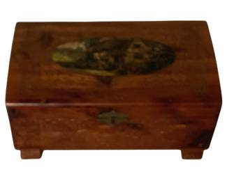 481 - Wooden Storage Box w/ Painted Lid 5"x11"x6" (Description): Wooden storage box featuring a hinged domed lid with a painted oval scenic medallion on top. The box is crafted from warm-toned wood with a polished finish and rests on four bracket feet. A decorative metal clasp adorns the front. Measures 5 inches by 11 inches by 6 inches.