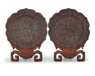 1258 A pair of Chinese cinnabar style trays 20th century or earlier Each carved with maker's mark verso Each depicting a figural scene of scholars examining a scroll, displayed in a carved wood stand 2 pieces Each tray: 9.375" Dia.; Each stand: 9.5" H x 6.625" W x 3.875" D Estimate: $100 - $200