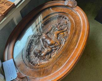 Add a touch of classic elegance to your home with this beautiful vintage tea table. It features an oval shape and beautiful wooden details. This is a perfect statement piece for a living room, parlor, or entryway.  The center features a gorgeous, deeply carved scene under the glass.  The top glass tray has two decorative handles so you can easily lift it up to serve guests.