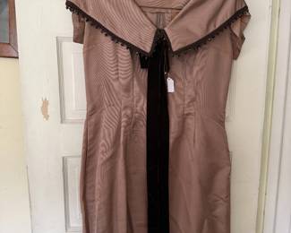  Step back in time with this stunning, classic cocktail dress!   Featuring a beautiful structured portrait collar adorned with delicate dark beaded trim, it channels pure mid-century sophistication. The center is accented with a rich, long black velvet tie ribbon that drops down the front for an elegant vertical line.