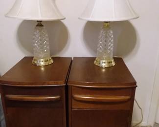 Wooden bedside tables accented with cut glass lamps with white shades. Light your way in luxury with these gorgeous lamps