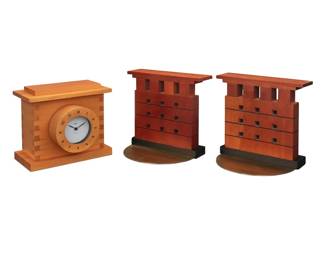 2184 Michael Graves (1934-2015) A table clock for Alessi and pair of bookends, 1990s Clock lid impressed: ALESSI / ITALY / DESIGN MICHAEL GRAVES; dial with printed signature: Graves Each bookend maple, ebonized wood, and brass, with a quartz movement clock 3 pieces Each bookend: 6.5" H x 7.5" W x 2" D; Clock: 6" H x 7" W x 5" D Estimate: $200 - $300