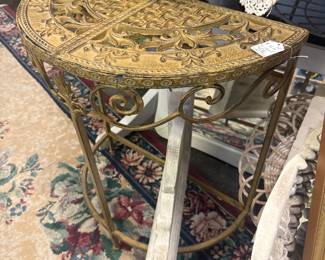 vintage-style cast iron demilune console table features an intricate, ornate scrollwork pattern in a distressed gold finish.
