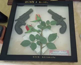 framed shadow box labeled "GUN'S & ROSES" containing a preserved rose and two small derringer pistols