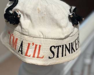 vintage-style white bucket hat features hand-stitched skunks and embroidered text that reads "I'm a L'il Stinker"