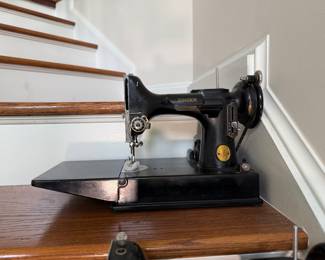 Vintage Singer Featherweight 221 sewing machine, recognized by its portable design and black finish with gold decals