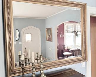 Large gilt-framed wall mirror over sideboard with candlesticks