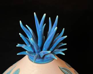 A502 - $100. Natalie Blake. Clay Vase with Blue Floral Flower Top. Measures 8" x 12.25" tall. Some flower tips have been repaired.